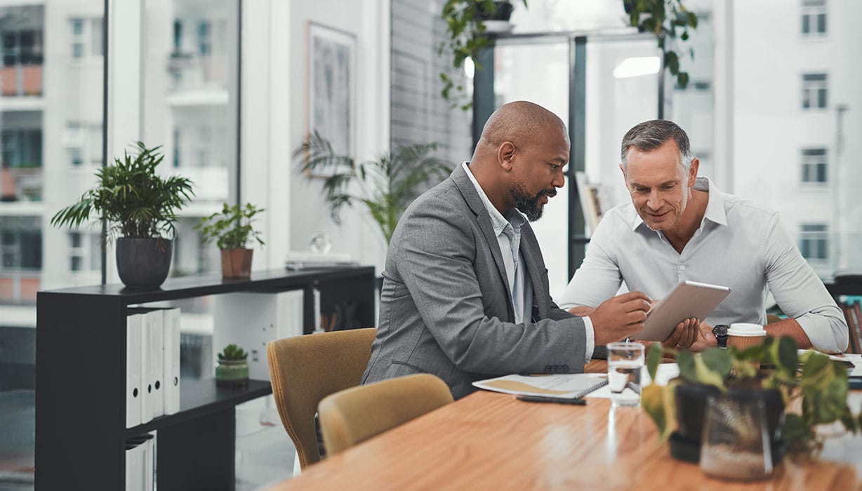two men in an office seated at a table looking at a pad of paper
